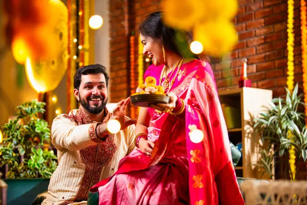 Tatlılar, Hediye Kutuları, Diwali Dekorasyonları, Diwali Festivali gecesi kanepede oturup Neşeyle Gülen Çiftler Birbirlerinden Tatlı Laddu Kapıyor