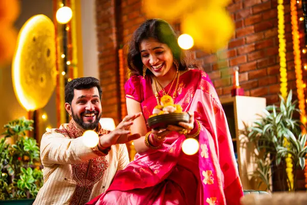 Tatlılar, Hediye Kutuları, Diwali Dekorasyonları, Diwali Festivali gecesi kanepede oturup Neşeyle Gülen Çiftler Birbirlerinden Tatlı Laddu Kapıyor