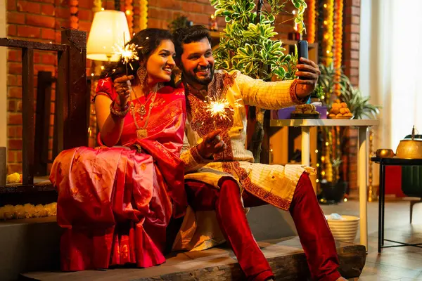 Video Çağrısında Sparklers 'ı tutan Hintli Genç Çift Geleneksel Şenlik Merdiveni' nde oturan Neşeli Diwali Akşamı 'nda gülümseyen kıvılcımlar sallarken Smartphone video çağrısına katıldılar