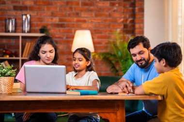 Ebeveynler evde çocuklara bilgisayar ve kitap öğretiyor, Hintli baba ve anne, oğullarına ev ödevlerinde, okumada, yazmada ve online çalışmada yardım ediyorlar.