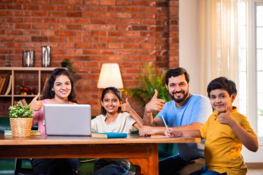 Ebeveynler evde çocuklara bilgisayar ve kitap öğretiyor, Hintli baba ve anne, oğullarına ev ödevlerinde, okumada, yazmada ve online çalışmada yardım ediyorlar.