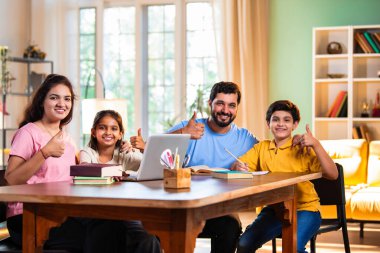 Ebeveynler evde çocuklara bilgisayar ve kitap öğretiyor, Hintli baba ve anne, oğullarına ev ödevlerinde, okumada, yazmada ve online çalışmada yardım ediyorlar.