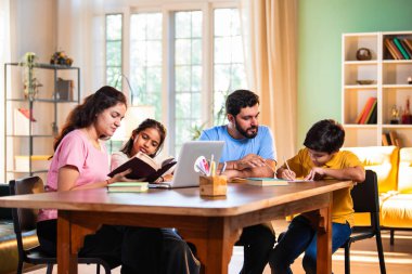 Ebeveynler evde çocuklara bilgisayar ve kitap öğretiyor, Hintli baba ve anne, oğullarına ev ödevlerinde, okumada, yazmada ve online çalışmada yardım ediyorlar.