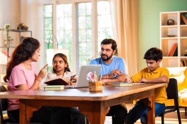 Ebeveynler evde çocuklara bilgisayar ve kitap öğretiyor, Hintli baba ve anne, oğullarına ev ödevlerinde, okumada, yazmada ve online çalışmada yardım ediyorlar.