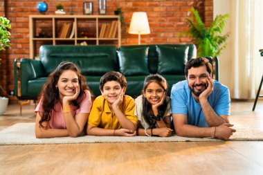 Aile çene üzerinde mutlu bir şekilde uzanmış, Hintli baba, anne, oğul, modern, müsrif oturma odasında kameraya bakıyor, evde birlikte rahatlıyor, bağ kuruyor ve eğleniyoruz.