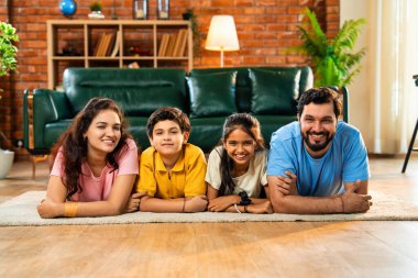 Aile çene üzerinde mutlu bir şekilde uzanmış, Hintli baba, anne, oğul, modern, müsrif oturma odasında kameraya bakıyor, evde birlikte rahatlıyor, bağ kuruyor ve eğleniyoruz.