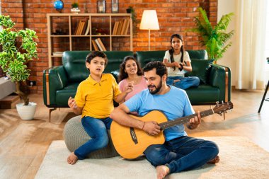 Babam gülen Hintli eş, oğul ve kızıyla gitar çalıyor. Müsrif oturma odasında oturuyor. Müzikal kaynaşmanın ve modern evde kaliteli zaman geçirmenin tadını çıkarıyor.