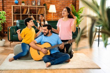 Babam gülen Hintli eş, oğul ve kızıyla gitar çalıyor. Müsrif oturma odasında oturuyor. Müzikal kaynaşmanın ve modern evde kaliteli zaman geçirmenin tadını çıkarıyor.