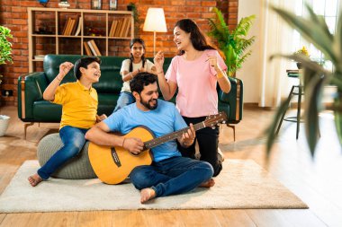 Babam gülen Hintli eş, oğul ve kızıyla gitar çalıyor. Müsrif oturma odasında oturuyor. Müzikal kaynaşmanın ve modern evde kaliteli zaman geçirmenin tadını çıkarıyor.