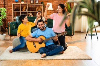 Babam gülen Hintli eş, oğul ve kızıyla gitar çalıyor. Müsrif oturma odasında oturuyor. Müzikal kaynaşmanın ve modern evde kaliteli zaman geçirmenin tadını çıkarıyor.