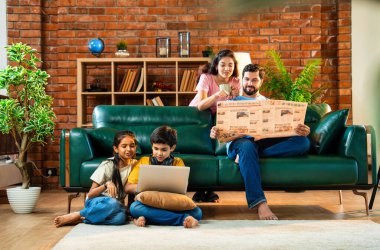 Çocuklar dizüstü bilgisayar kullanıyor, babaları gazete okuyor aileleriyle rahat bir koltukta oturuyor, kızları ve oğulları olan Asyalı genç bir çift modern Hint evinde teknoloji ve basılı medyayla meşgul.