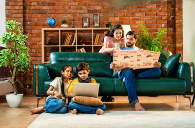 Çocuklar dizüstü bilgisayar kullanıyor, babaları gazete okuyor aileleriyle rahat bir koltukta oturuyor, kızları ve oğulları olan Asyalı genç bir çift modern Hint evinde teknoloji ve basılı medyayla meşgul.