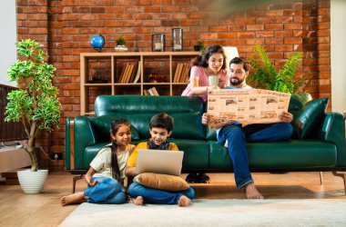 Çocuklar dizüstü bilgisayar kullanıyor, babaları gazete okuyor aileleriyle rahat bir koltukta oturuyor, kızları ve oğulları olan Asyalı genç bir çift modern Hint evinde teknoloji ve basılı medyayla meşgul.