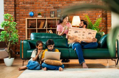 Çocuklar dizüstü bilgisayar kullanıyor, babaları gazete okuyor aileleriyle rahat bir koltukta oturuyor, kızları ve oğulları olan Asyalı genç bir çift modern Hint evinde teknoloji ve basılı medyayla meşgul.