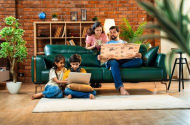 Çocuklar dizüstü bilgisayar kullanıyor, babaları gazete okuyor aileleriyle rahat bir koltukta oturuyor, kızları ve oğulları olan Asyalı genç bir çift modern Hint evinde teknoloji ve basılı medyayla meşgul.