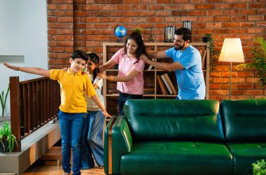 Mutlu Hintli aile içeride tren oyunu oynuyor, küçük çocuk motor gibi yol gösteriyor, ebeveynler de onu takip ediyor, evde rahat bir oturma odasında birlikte koşarken eğleniyorlar.