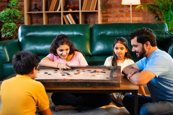 Hintli ebeveynler küçük çocuklarla kapalı mekanlarda vakit geçirmekten zevk alırken, masa başı eğlencesi üzerine bağ kurarak tahta disklere vurmayı hedefleyen aile birlikte carrom masası oyunu oynuyor.