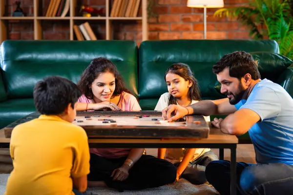 Hintli ebeveynler küçük çocuklarla kapalı mekanlarda vakit geçirmekten zevk alırken, masa başı eğlencesi üzerine bağ kurarak tahta disklere vurmayı hedefleyen aile birlikte carrom masası oyunu oynuyor.