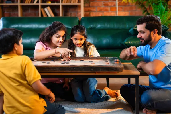 Hintli ebeveynler küçük çocuklarla kapalı mekanlarda vakit geçirmekten zevk alırken, masa başı eğlencesi üzerine bağ kurarak tahta disklere vurmayı hedefleyen aile birlikte carrom masası oyunu oynuyor.