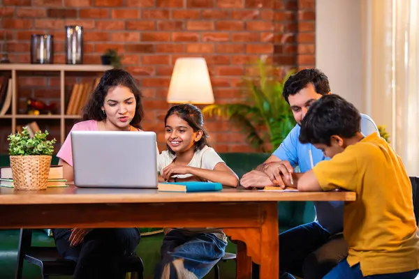 Ebeveynler evde çocuklara bilgisayar ve kitap öğretiyor, Hintli baba ve anne, oğullarına ev ödevlerinde, okumada, yazmada ve online çalışmada yardım ediyorlar.