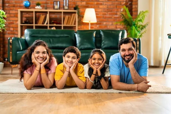 Aile çene üzerinde mutlu bir şekilde uzanmış, Hintli baba, anne, oğul, modern, müsrif oturma odasında kameraya bakıyor, evde birlikte rahatlıyor, bağ kuruyor ve eğleniyoruz.