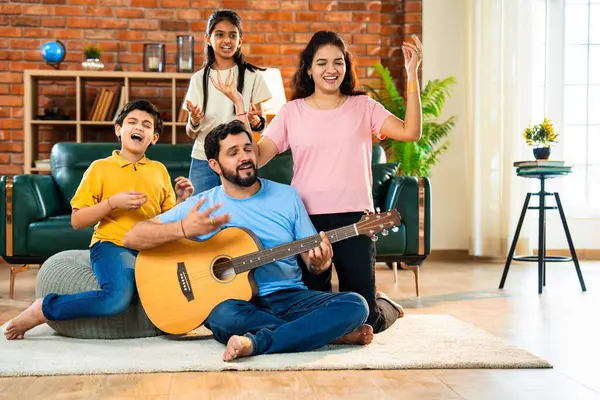 Babam gülen Hintli eş, oğul ve kızıyla gitar çalıyor. Müsrif oturma odasında oturuyor. Müzikal kaynaşmanın ve modern evde kaliteli zaman geçirmenin tadını çıkarıyor.