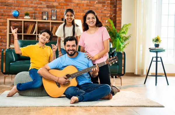 Babam gülen Hintli eş, oğul ve kızıyla gitar çalıyor. Müsrif oturma odasında oturuyor. Müzikal kaynaşmanın ve modern evde kaliteli zaman geçirmenin tadını çıkarıyor.