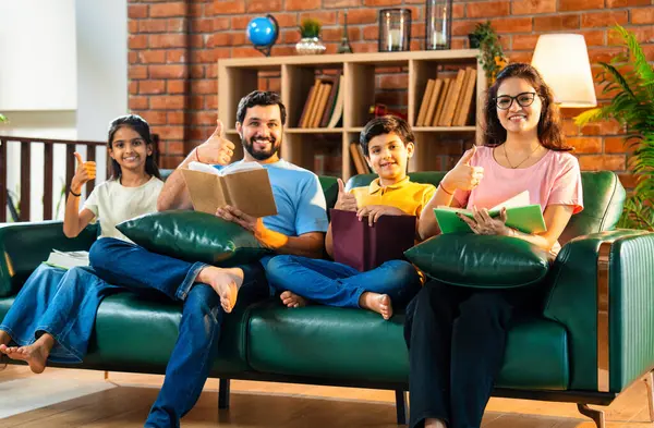 Aile kitap tanıtımını evde rahat bir kanepede otururken yapıyor. Çocuklu Asyalı genç bir çift okuma alışkanlığı geliştirmenin önemini anlatıyor. Zeka ve iç mekanda gelişim.