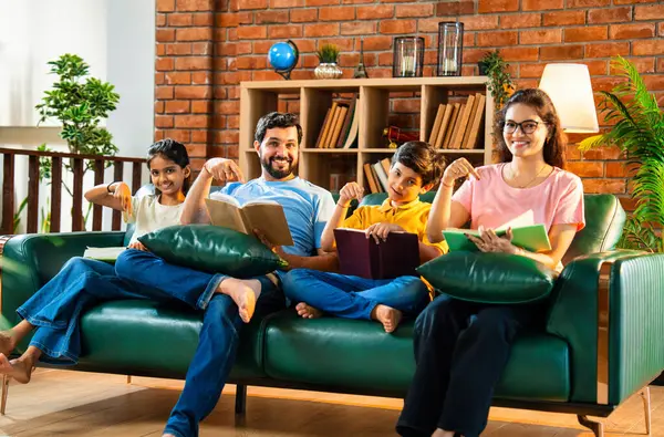 Aile kitap tanıtımını evde rahat bir kanepede otururken yapıyor. Çocuklu Asyalı genç bir çift okuma alışkanlığı geliştirmenin önemini anlatıyor. Zeka ve iç mekanda gelişim.