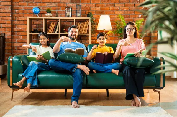 Aile kitap tanıtımını evde rahat bir kanepede otururken yapıyor. Çocuklu Asyalı genç bir çift okuma alışkanlığı geliştirmenin önemini anlatıyor. Zeka ve iç mekanda gelişim.