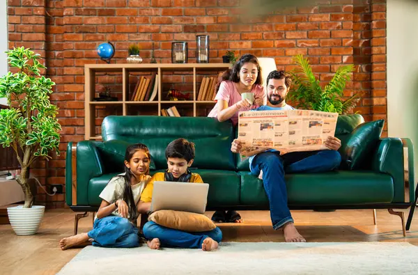 Çocuklar dizüstü bilgisayar kullanıyor, babaları gazete okuyor aileleriyle rahat bir koltukta oturuyor, kızları ve oğulları olan Asyalı genç bir çift modern Hint evinde teknoloji ve basılı medyayla meşgul.