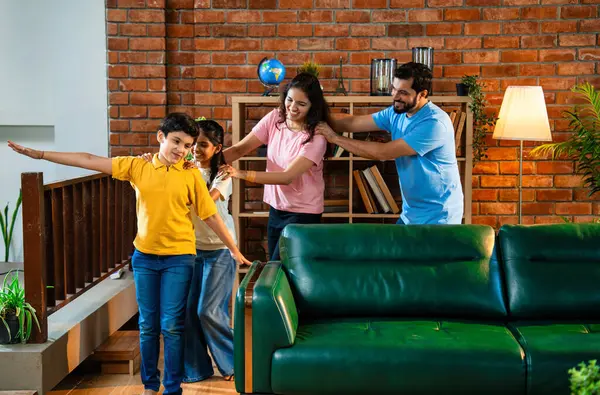 Mutlu Hintli aile içeride tren oyunu oynuyor, küçük çocuk motor gibi yol gösteriyor, ebeveynler de onu takip ediyor, evde rahat bir oturma odasında birlikte koşarken eğleniyorlar.