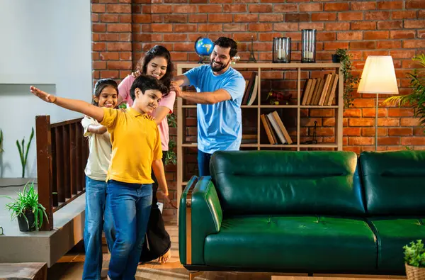 Mutlu Hintli aile içeride tren oyunu oynuyor, küçük çocuk motor gibi yol gösteriyor, ebeveynler de onu takip ediyor, evde rahat bir oturma odasında birlikte koşarken eğleniyorlar.