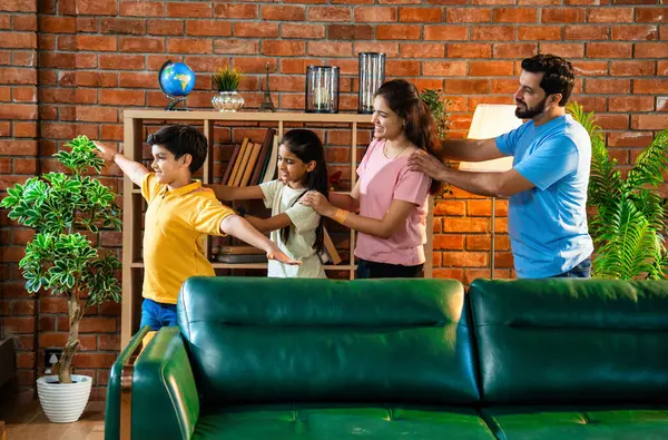 Mutlu Hintli aile içeride tren oyunu oynuyor, küçük çocuk motor gibi yol gösteriyor, ebeveynler de onu takip ediyor, evde rahat bir oturma odasında birlikte koşarken eğleniyorlar.