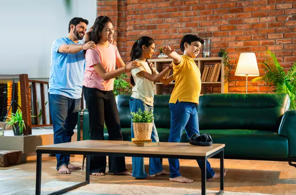 Mutlu Hintli aile içeride tren oyunu oynuyor, küçük çocuk motor gibi yol gösteriyor, ebeveynler de onu takip ediyor, evde rahat bir oturma odasında birlikte koşarken eğleniyorlar.