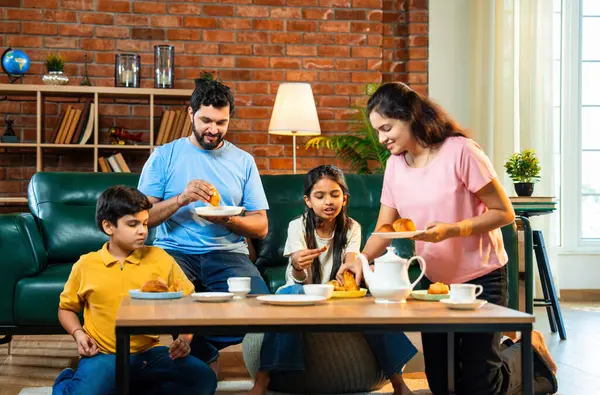 Hintli aile evde çayla samosa atıştırmalıkları yiyor, ebeveynler ve çocuklar sıcak oturma odasında oturmuş sohbet ederken, gülerken ve kaliteli bir bağ kurma zamanı geçirirken kızarmış yiyecek ve içeceklerin tadını çıkarıyorlar.