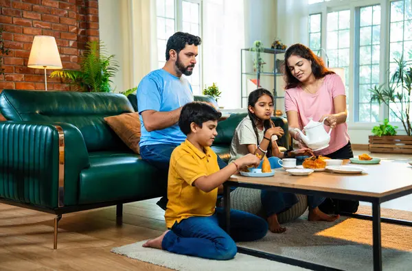 Hintli aile evde çayla samosa atıştırmalıkları yiyor, ebeveynler ve çocuklar sıcak oturma odasında oturmuş sohbet ederken, gülerken ve kaliteli bir bağ kurma zamanı geçirirken kızarmış yiyecek ve içeceklerin tadını çıkarıyorlar.