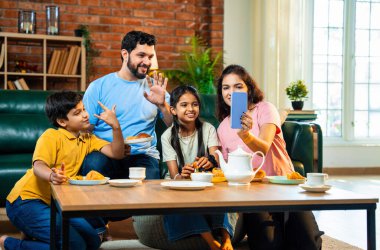 Evde samosa yiyip çay içerken görüntülü konuşma, çocuklu Hintli aileler arkadaşlarıyla ya da akrabalarıyla sohbet etme, rahat modern oturma odasında atıştırmalıkların tadını çıkarma.