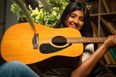 Kederli Lamba ile Sıcak Oda 'da Otururken Gitarlı Kız Pozu Tuğla Duvara Karşı Huysuz Lamba, Hint Genç Müzisyen Yazı, Beste veya Evde Evde Yalnız Akustik Müzik Çalıyor