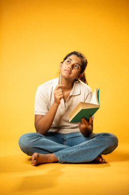 Kitap yazmakta, Hintli Asyalı Kız Derinlemesine Düşünerek Oturmakta ve Ders Çalışırken Not Almakta, Odaklanma ve Merakı Göstermekte Öğrenme veya Ödevde Etkinlik Göstermekte