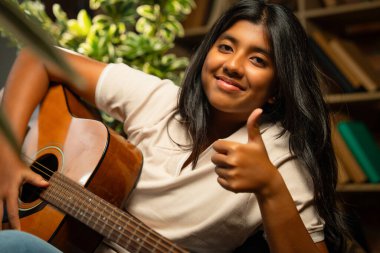 Kederli Lamba ile Sıcak Oda 'da Otururken Gitarlı Kız Pozu Tuğla Duvara Karşı Huysuz Lamba, Hint Genç Müzisyen Yazı, Beste veya Evde Evde Yalnız Akustik Müzik Çalıyor