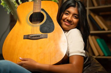 Kederli Lamba ile Sıcak Oda 'da Otururken Gitarlı Kız Pozu Tuğla Duvara Karşı Huysuz Lamba, Hint Genç Müzisyen Yazı, Beste veya Evde Evde Yalnız Akustik Müzik Çalıyor