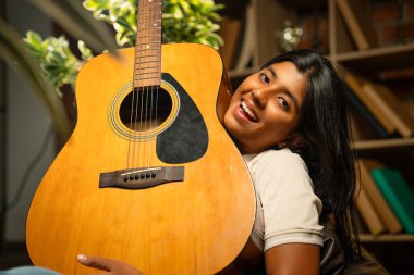 Kederli Lamba ile Sıcak Oda 'da Otururken Gitarlı Kız Pozu Tuğla Duvara Karşı Huysuz Lamba, Hint Genç Müzisyen Yazı, Beste veya Evde Evde Yalnız Akustik Müzik Çalıyor