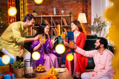 Soğuk bir içecekle Diwali kutlaması, Hintli genç evli çift ve geleneksel şenlik kıyafetleriyle Hindu festivalini süslenmiş evde portakal suyu veya meyve suyuyla kutluyorlar.