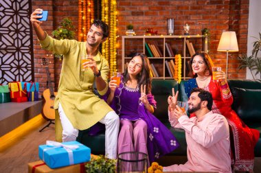 Soğuk içecekle Diwali selfie, Hintli genç evli çiftler geleneksel festival kıyafetleriyle evde Deepavali bayramını kutluyorlar, akıllı telefonla neşeyi yakalıyorlar, içki içiyorlar.