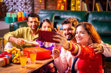 Arkadaşlarıyla Diwali selfie çeken Hindu genç evli çift Hindu festivali Deepavali 'yi kutlamak için dekore edilmiş evde laddu barfi şekerlerini tıklayarak selfie çekiyor.