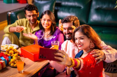 Arkadaşlarıyla Diwali selfie çeken Hindu genç evli çift Hindu festivali Deepavali 'yi kutlamak için dekore edilmiş evde laddu barfi şekerlerini tıklayarak selfie çekiyor.