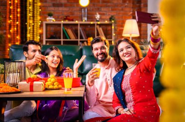 Arkadaşlarıyla Diwali selfie çeken Hindu genç evli çift Hindu festivali Deepavali 'yi kutlamak için dekore edilmiş evde laddu barfi şekerlerini tıklayarak selfie çekiyor.