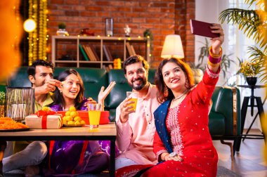 Arkadaşlarıyla Diwali selfie çeken Hindu genç evli çift Hindu festivali Deepavali 'yi kutlamak için dekore edilmiş evde laddu barfi şekerlerini tıklayarak selfie çekiyor.