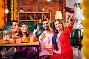 Arkadaşlarıyla Diwali selfie çeken Hindu genç evli çift Hindu festivali Deepavali 'yi kutlamak için dekore edilmiş evde laddu barfi şekerlerini tıklayarak selfie çekiyor.